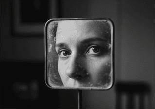 زنی که با نگرانی به افتادگی پلک خود در آینه نگاه می‌کند و به دنبال درمان است.